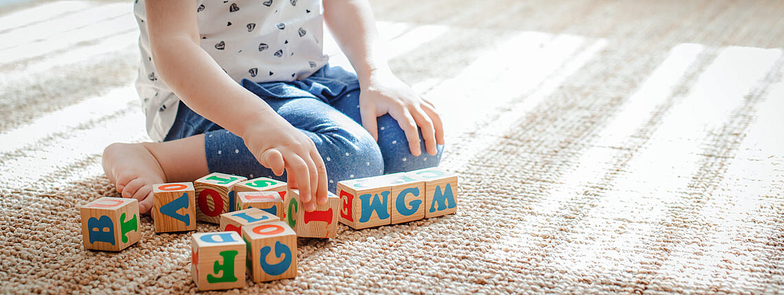 Kind spielt mit Holzklötzen mit Buchstaben auf dem Boden im Zimmer ein kleines Mädchen baut einen Turm zu Hause oder im Kindergarten.