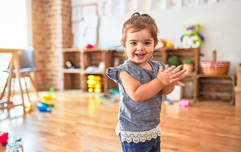 Schönes Kleinkind steht auf dem Boden und applaudiert und lächelt im Kindergarten