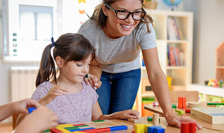 Erzieherin mit Kindern, die mit buntem didaktischem Holzspielzeug im Kindergarten spielen