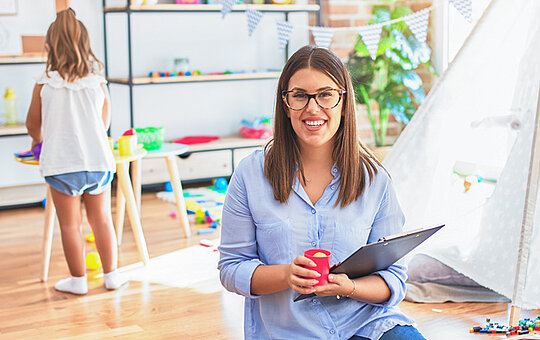 Kindergärtnerin mit Kleinkind im Hintergrund in einem Kindergarten Innenraum