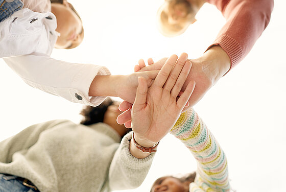 Kinder und Erwachsene legen als Zeichen des Zusammenhaltes die Hände übereinander in der Kita