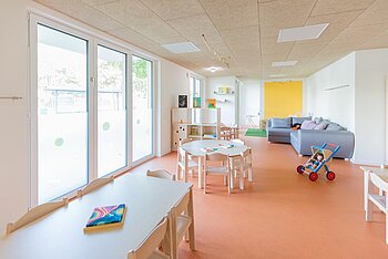 Gruppenraum mit Tischen und Spielecke der Kita Kleine Riesen München Neuperlach-Zentrum