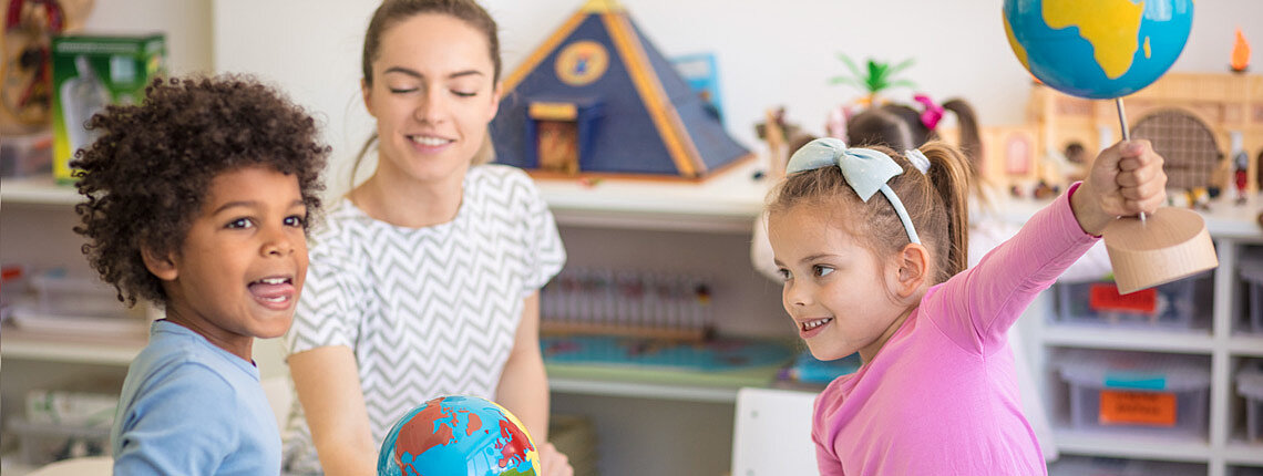 Zwei Kinder mit Globus und eine Erzieherin im Hintergrund