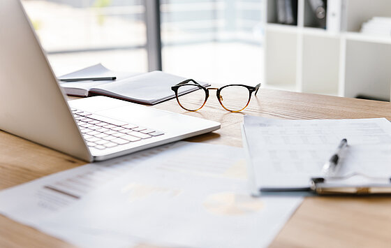 Arbeitsplatz einer Kita-Leitung mit einem Laptop, Notizen und einer abgelegten Brille