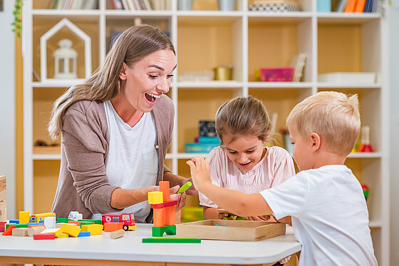 Erzieherin sitzt mit Kindern am Tisch und spielt