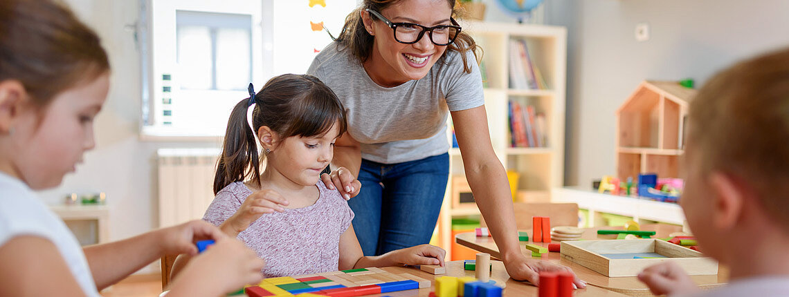 Erzieherin mit Kindern, die mit buntem didaktischem Holzspielzeug im Kindergarten spielen