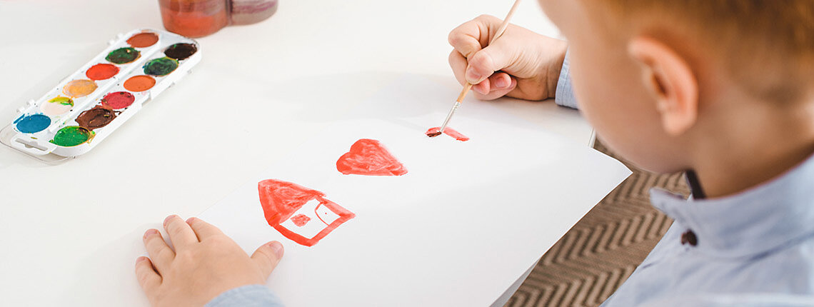Teilansicht eines Vorschülers mit roten Haaren, der ein Bild am Tisch im Klassenzimmer zeichnet